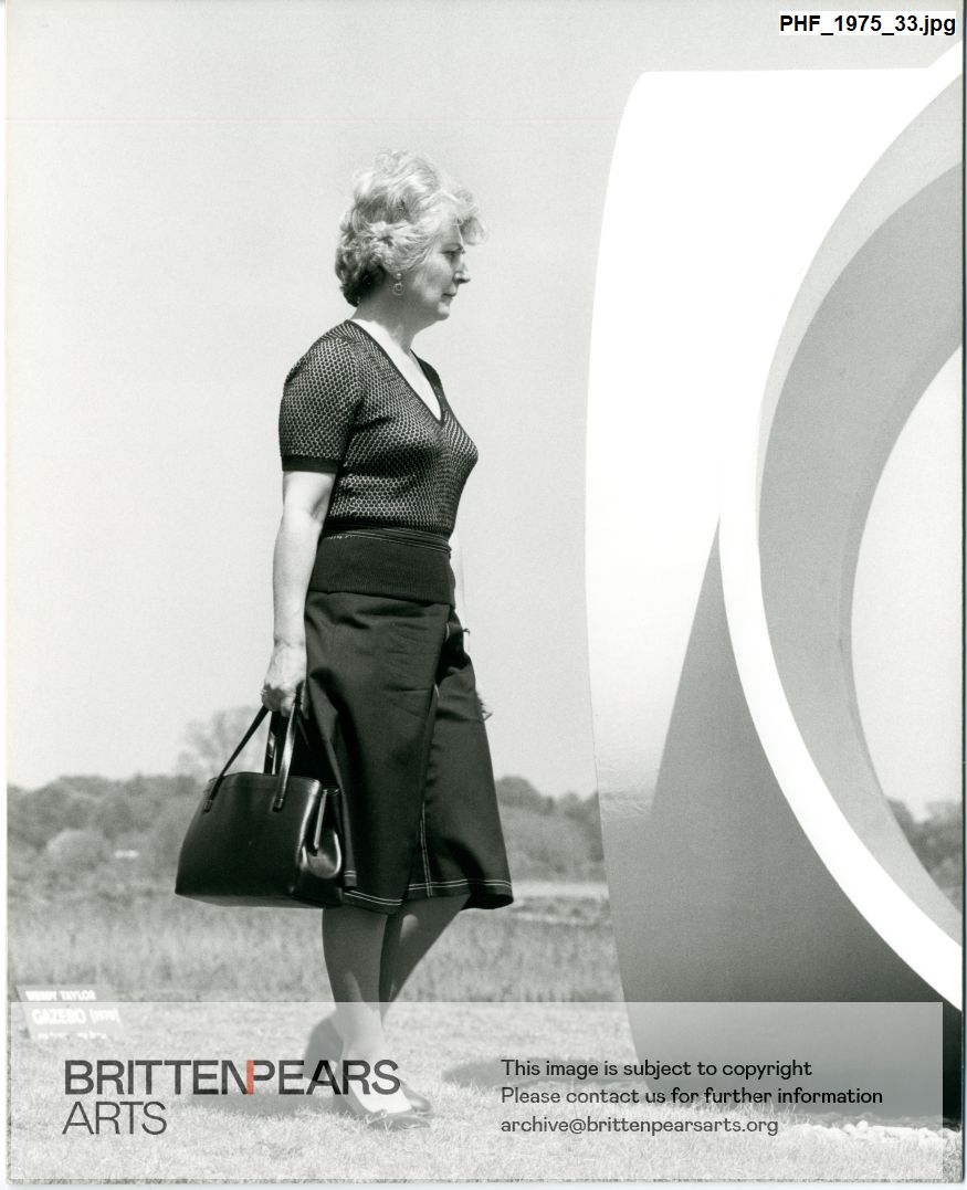 Photograph of Helen Watts standing by Wendy Taylor's sculpture Gazebo