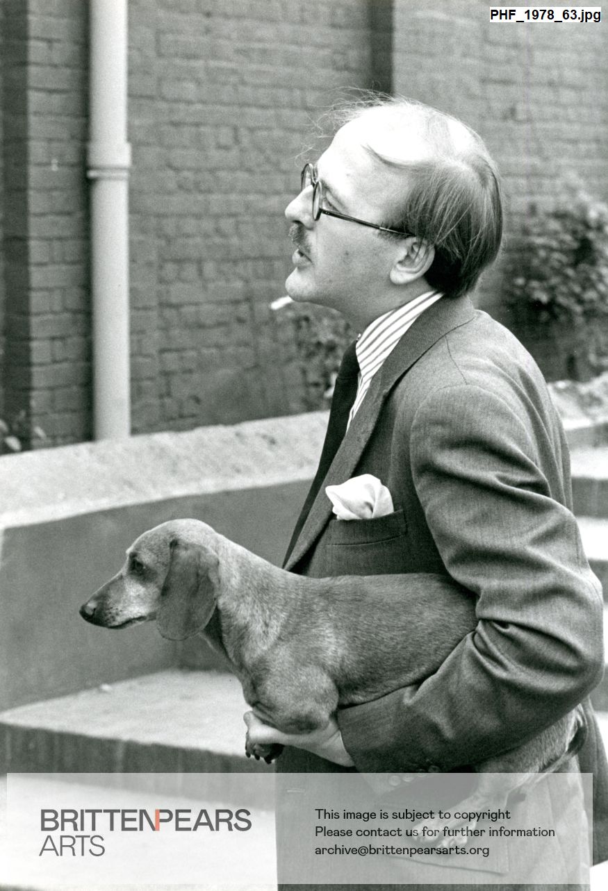 Photograph of an unidentified man carrying small dachshund dog